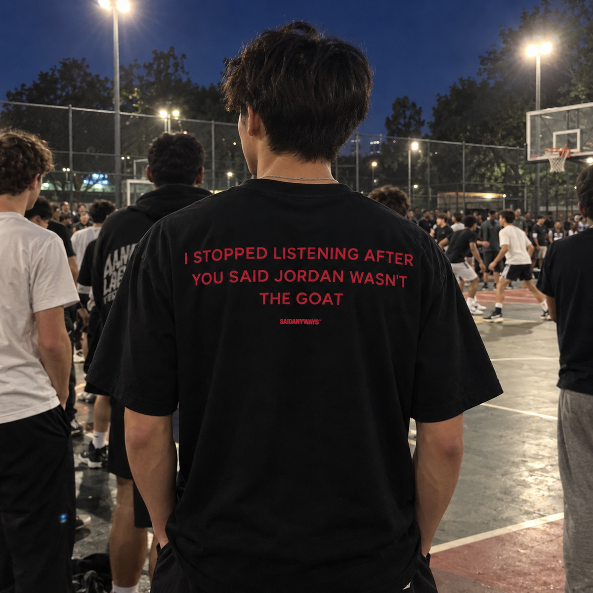 I Stopped Listening After You Said Jordan Wasn't The GOAT black tee, worn in a crowd at a basketball court